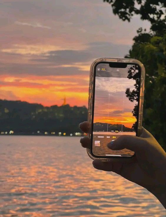 Capturing a vibrant sunset over water with a smartphone, showcasing nature's beauty and technology's role.