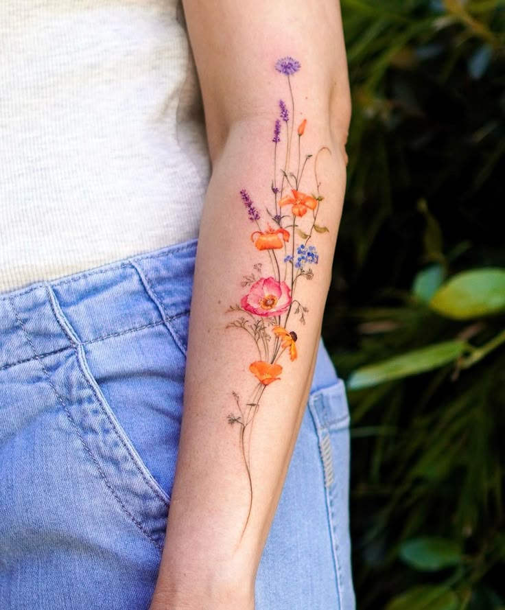 Floral tattoo on forearm with vibrant poppies and lavender, showcasing detailed artistry against a natural backdrop.