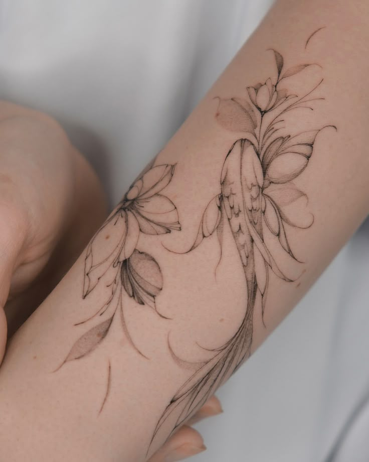 Delicate floral and bird tattoo design on forearm, showcasing intricate black ink detailing.