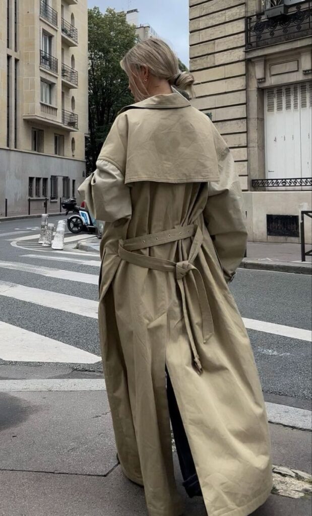 Woman in beige trench coat walking on a city street, showcasing urban fashion and style.