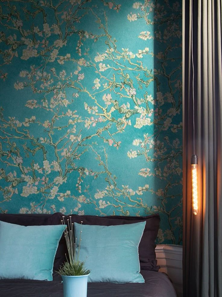 Bedroom with floral teal wallpaper, turquoise pillows, and a vertical pendant light.