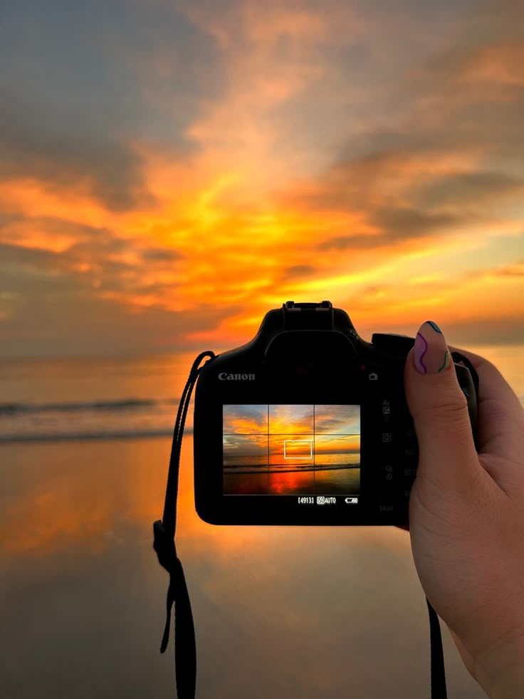 Camera capturing vibrant beach sunset, with orange sky reflection in ocean waves.