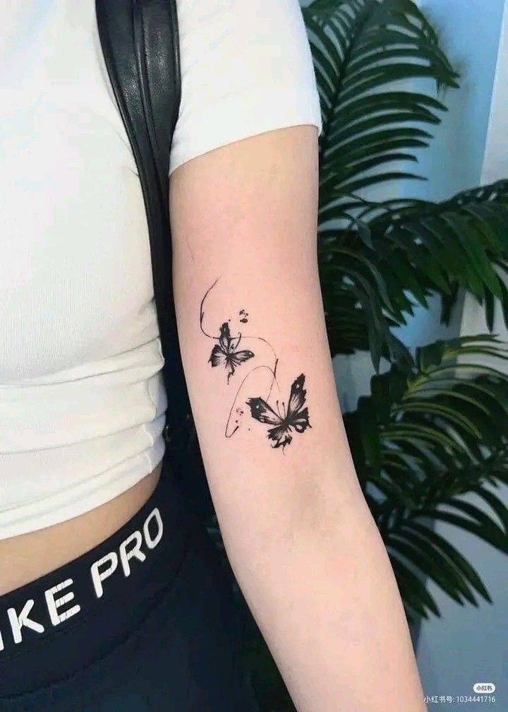 Butterfly tattoo on woman's arm with leaves in the background.