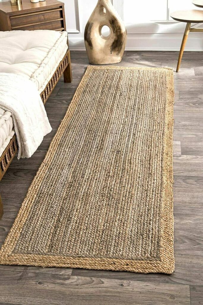 Natural jute rug on wooden floor in cozy, modern room with wicker chair and decorative vase.