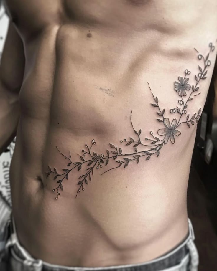 Floral vine rib tattoo on a toned torso, showcasing delicate flower and leaf details.