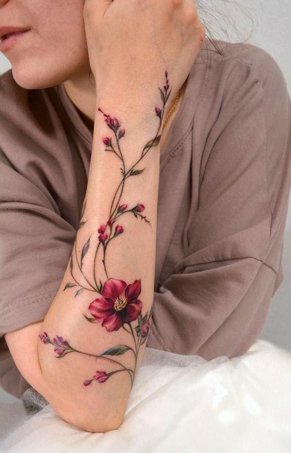 Floral arm tattoo with vibrant red flowers and delicate branches, showcasing intricate and elegant design.