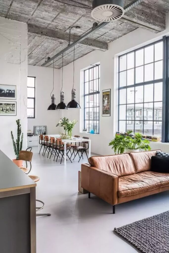 Industrial-style loft with leather sofa, hanging lights, and large windows. Modern interior design.