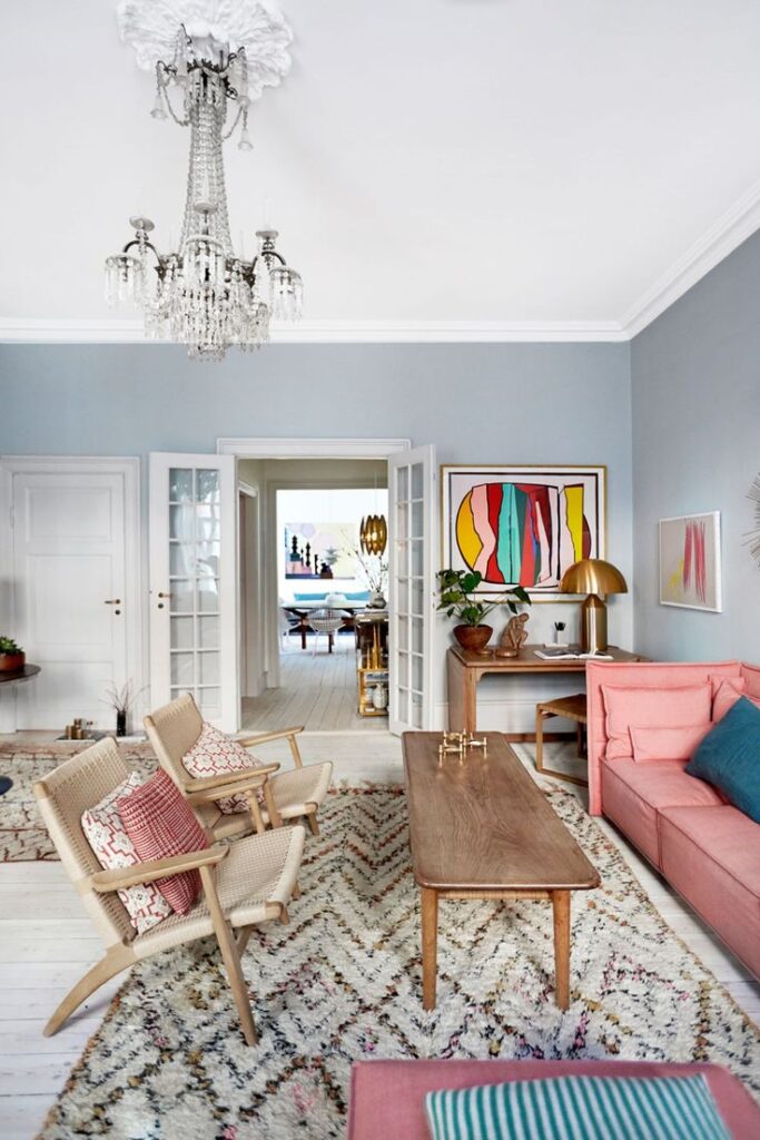 Stylish living room with colorful art, chandelier, wooden furniture, and pink sofa in a cozy Scandinavian design.