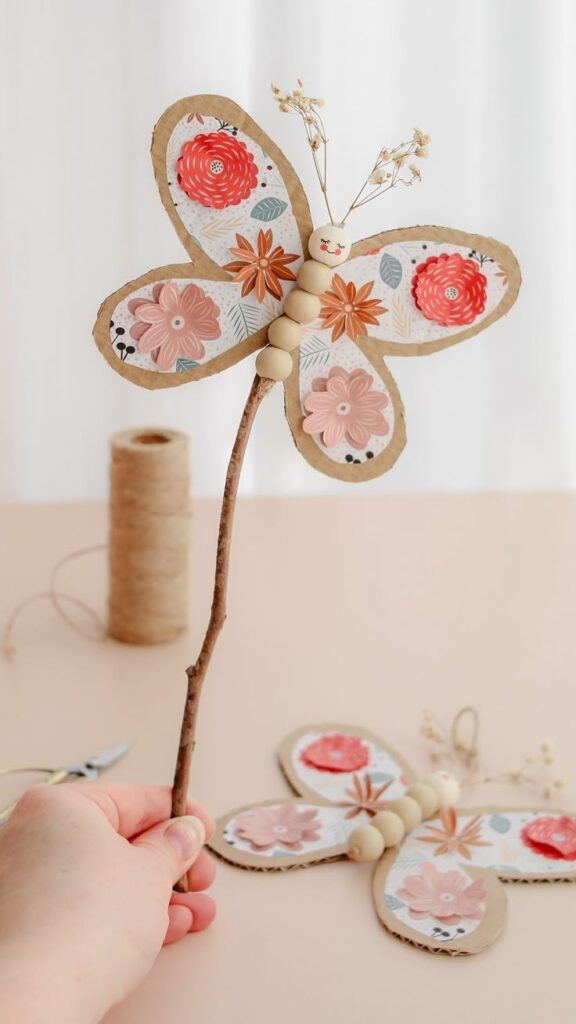 Handmade floral butterfly craft on stick with twine and scissors in background. Perfect for DIY decor projects.