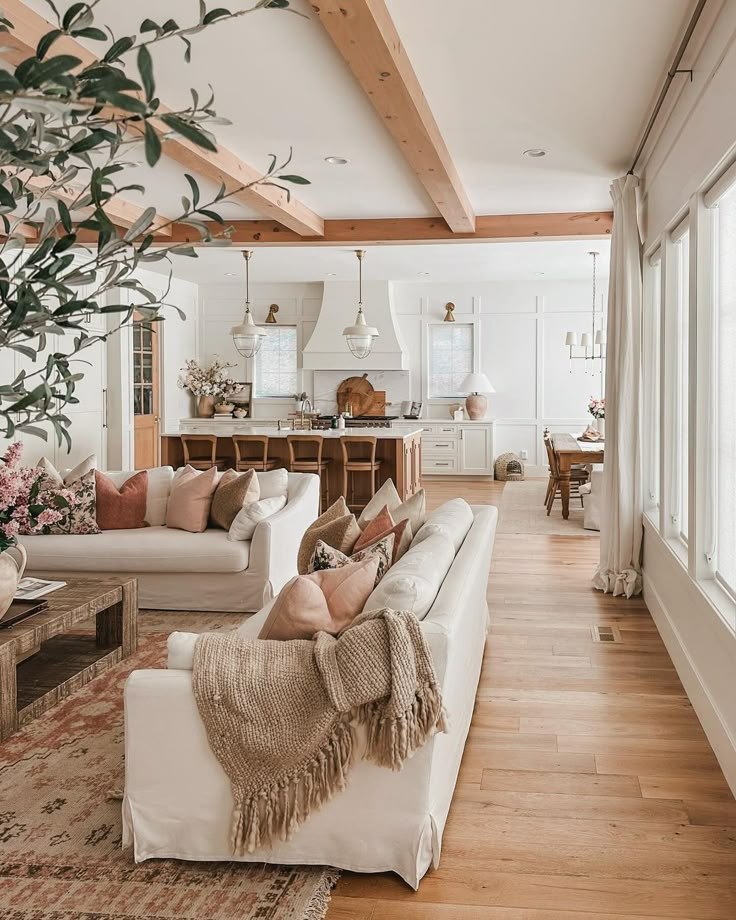 Spacious, cozy living room with white sofas, wooden beams, and modern kitchen, featuring warm, inviting decor.