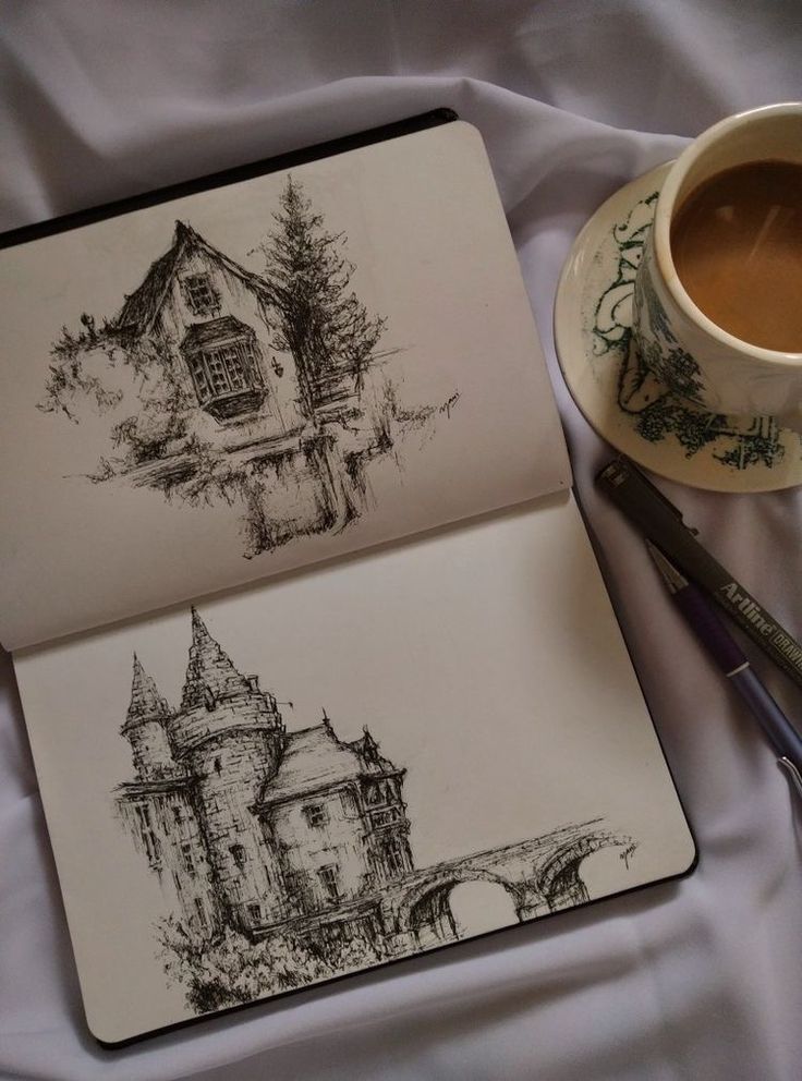 Sketchbook with pen drawings of a cottage and a castle, beside a cup of coffee on a saucer.