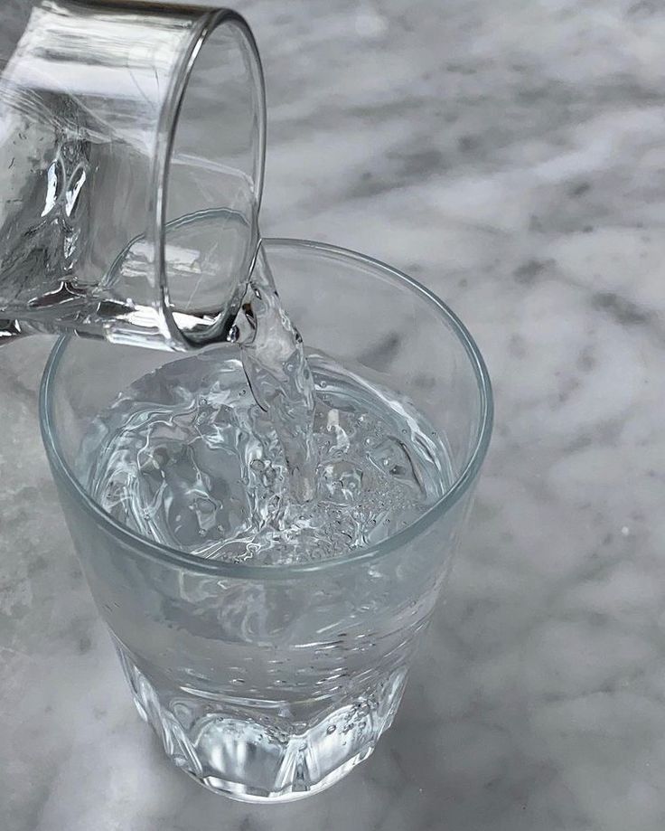 Glass of water being poured from a pitcher on a marble surface. Refreshing hydration concept.