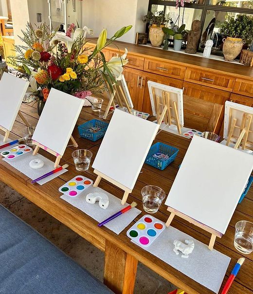 Art class setup with easels, paint palettes, and brushes on a wooden table, ready for a painting session.