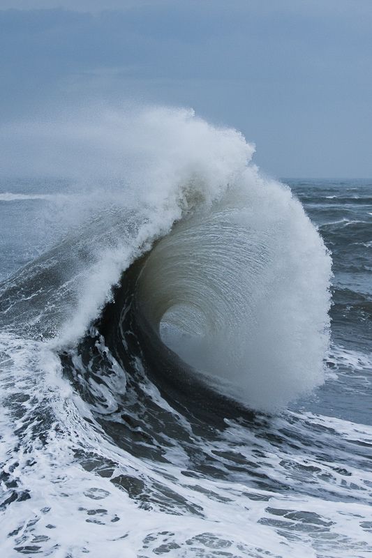 Powerful ocean wave curling with white sea foam under a cloudy sky.