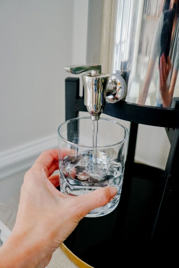 Hand holding glass filling with water from dispenser.