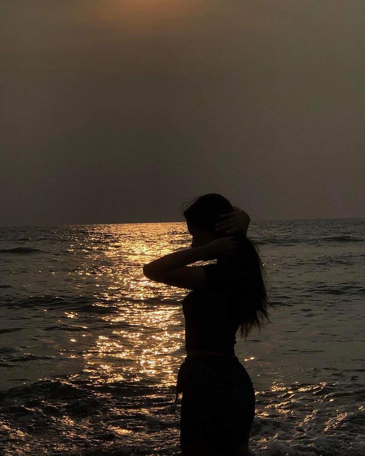 Silhouette of a woman by the sea at sunset, with golden reflections on the water.