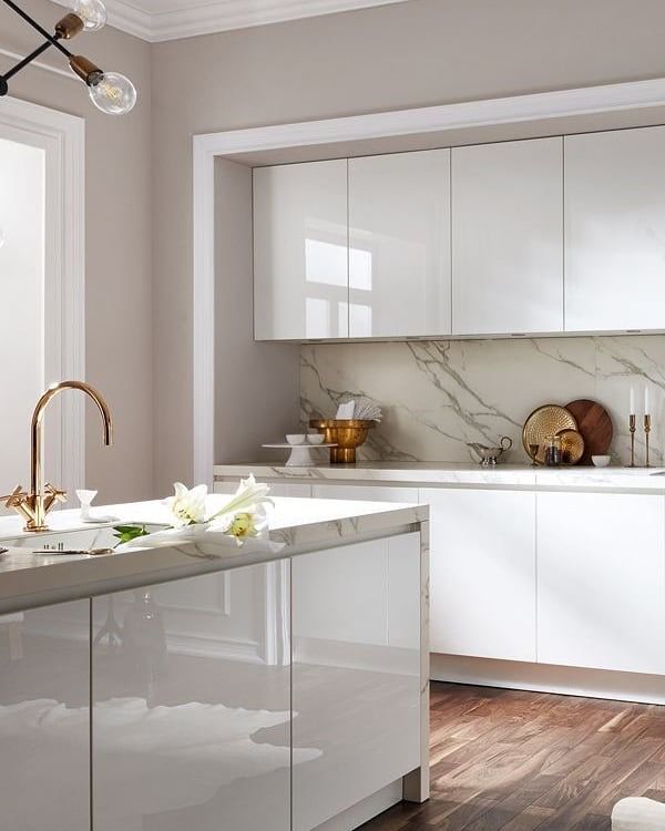 Modern white kitchen with marble countertops, gold faucet, and wooden floor. Minimalist design with elegant decor elements.