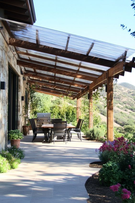 Covered patio with dining set overlooking scenic hills and greenery, stone wall on the side, vibrant flowers in foreground.