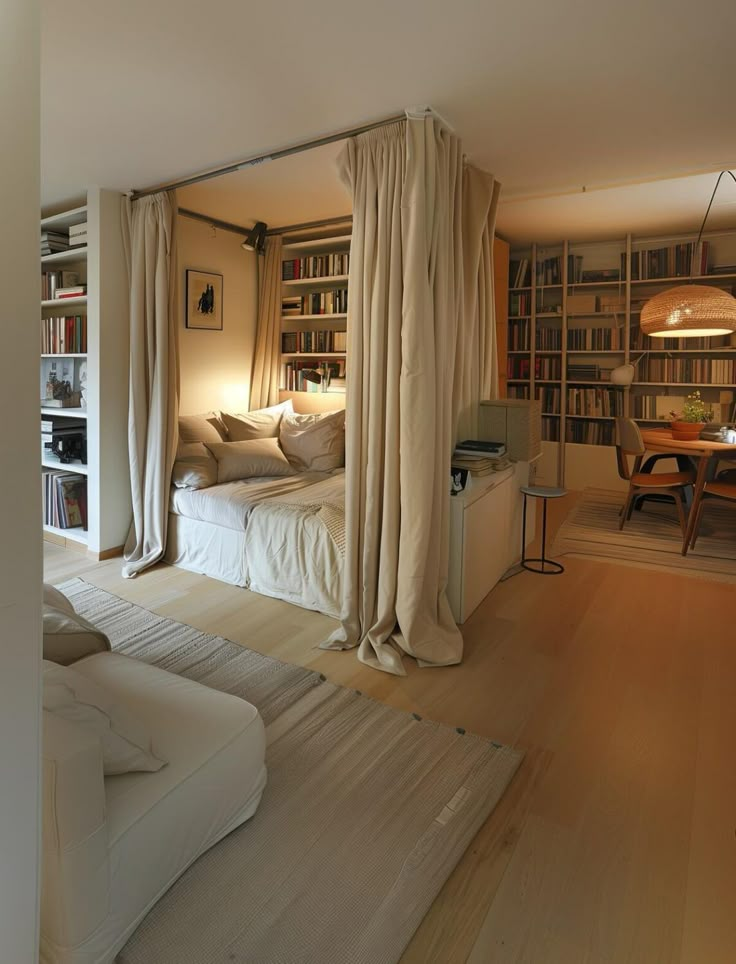 Cozy bedroom with beige curtains, bookshelves, and soft lighting next to a dining area with a woven pendant lamp.