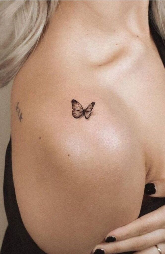 Close-up of a small butterfly tattoo on a woman's shoulder, showcasing minimalist ink design.