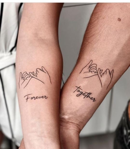 Matching forearm tattoos of intertwined pinky fingers with Forever and Together text, symbolizing love and unity.