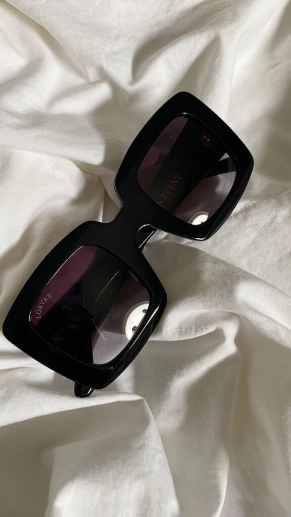 Stylish black square sunglasses with a glossy finish on white fabric.