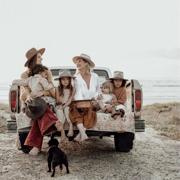 Family enjoying a day at the beach sitting on a truck tailgate with ocean view, wearing hats, boho style.