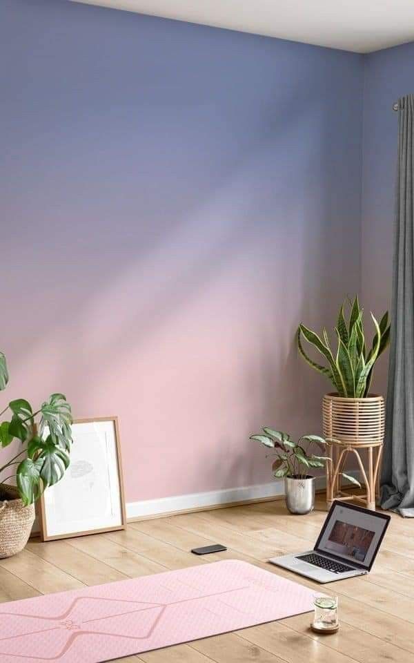 Home yoga space with pink mat, laptop, plants, and pastel wall background for relaxation and fitness exercises.