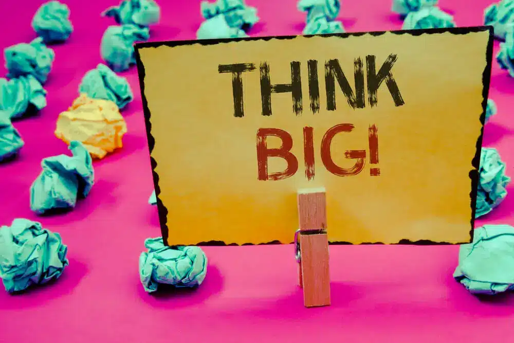 Sign with Think Big! surrounded by crumpled paper on a pink background, inspiring creativity and ambitious thinking.