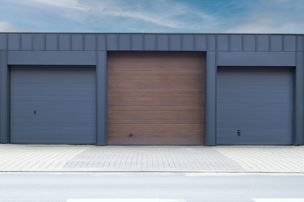 Modern garage with three doors, featuring sleek design and contrasting colors, under a clear blue sky.