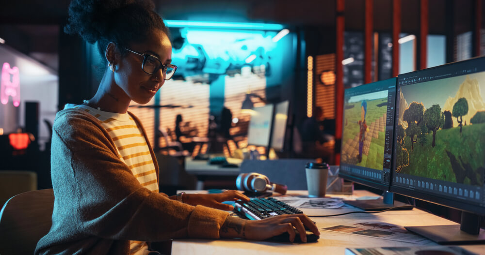 Woman designing a 3D video game environment on dual monitors in a modern office.