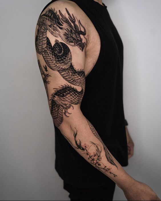 Arm with intricate black dragon tattoo in sleeveless black shirt, showcasing detailed tattoo artistry.