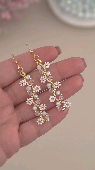 Delicate floral earrings with pearls and crystal beads on gold wire, resting gently on an open palm.