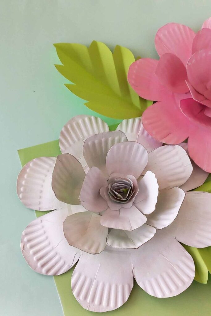 Paper flowers with white petals and green leaves on a pastel background.