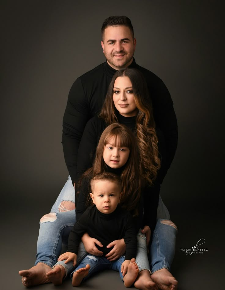 Happy family portrait with parents, daughter, and son in casual outfits, posing against a dark background.