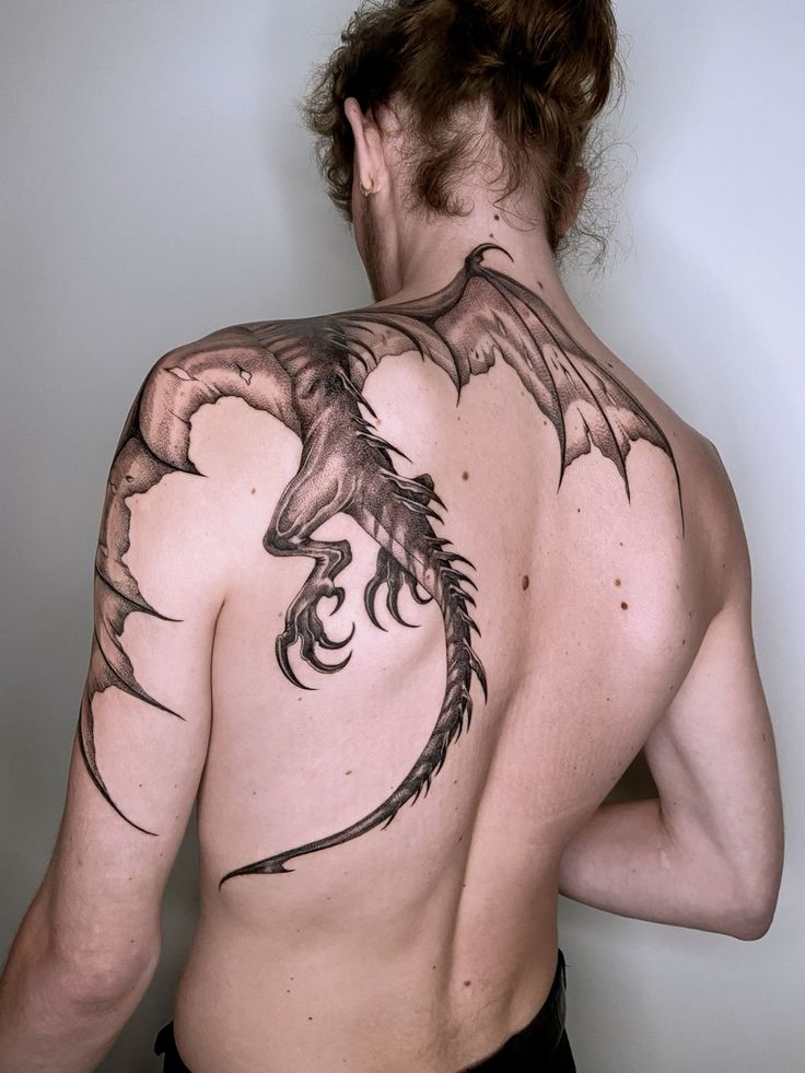 Dragon tattoo art on man's back, intricate design with wings extending across shoulder.