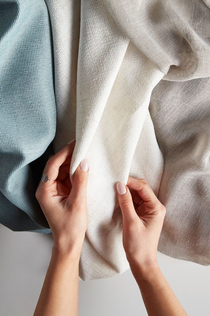 Hands touching soft, textured fabric swatches in beige and teal, showcasing textile quality and design choices.