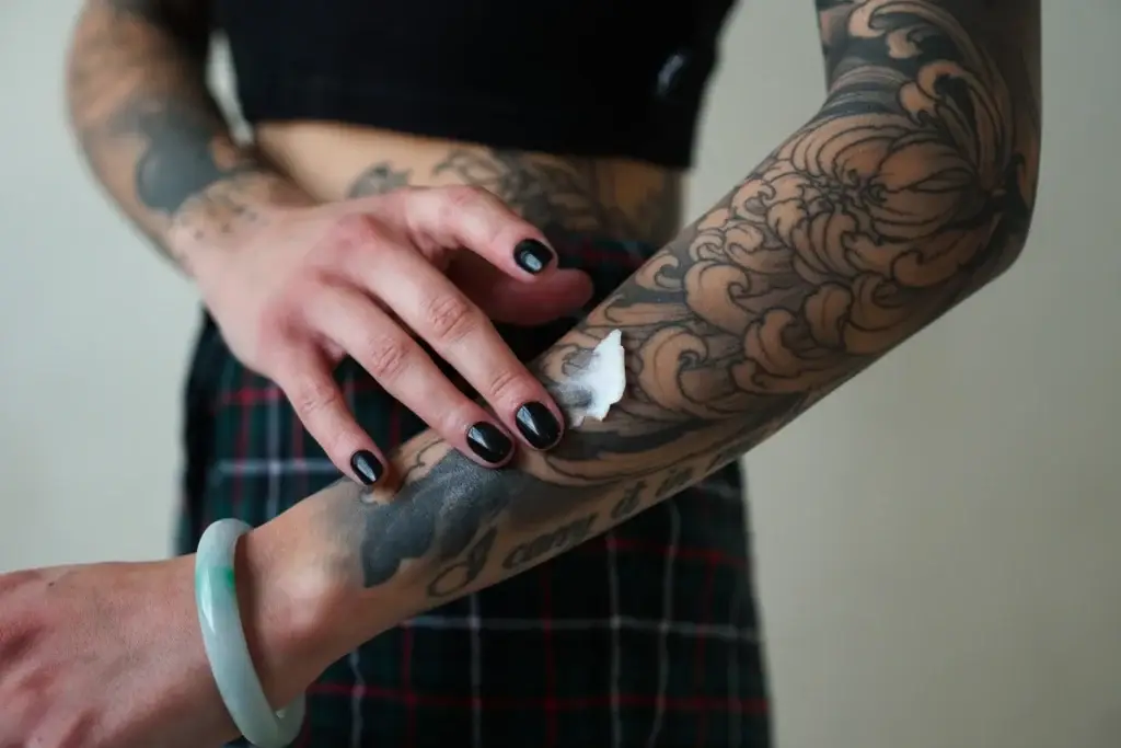 Person applying cream on tattooed arm for skincare and tattoo maintenance.