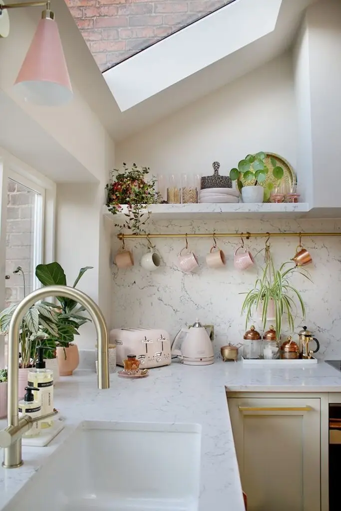 Modern kitchen with marble countertops, pink appliances, plants, and skylight for natural lighting. Cozy and stylish decor.