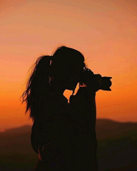 Silhouette of a person photographing a sunset with an orange sky in the background.