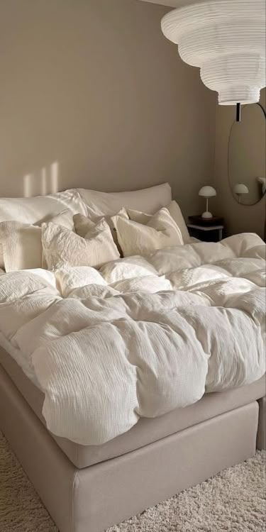 Cozy bedroom with beige decor, featuring a plush comforter, white pillows, and stylish hanging lamp.