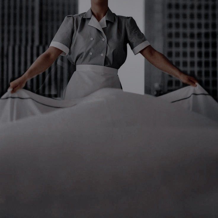 Housekeeper making a bed in uniform, smoothing a white sheet. Hotel room tidying, professional cleaning service.