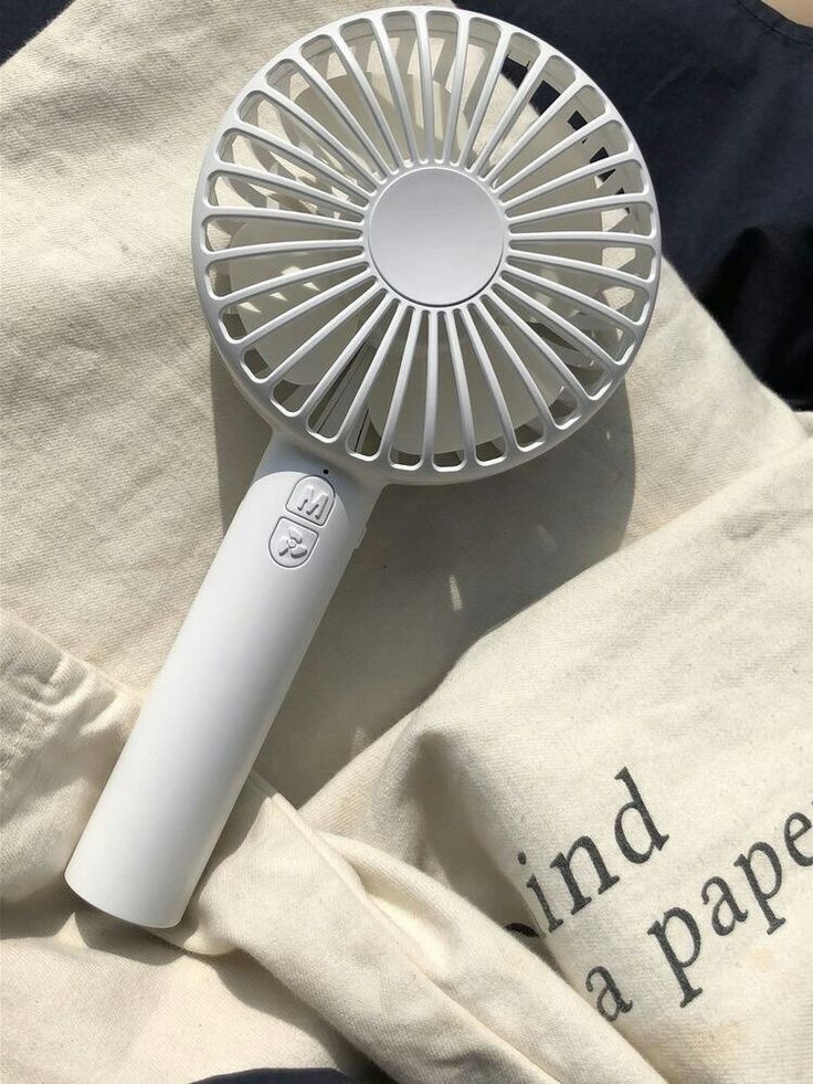 White handheld fan on a fabric surface in sunlight, ideal for portable cooling solutions.