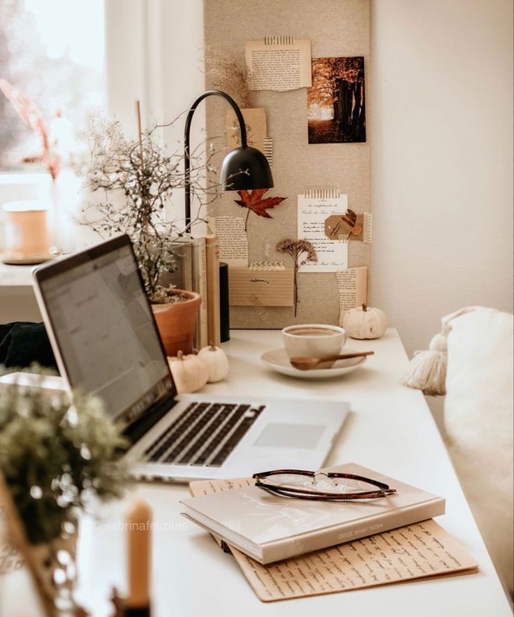 Cozy home office setup with laptop, books, glasses, and autumn decor, perfect for productivity and relaxation.