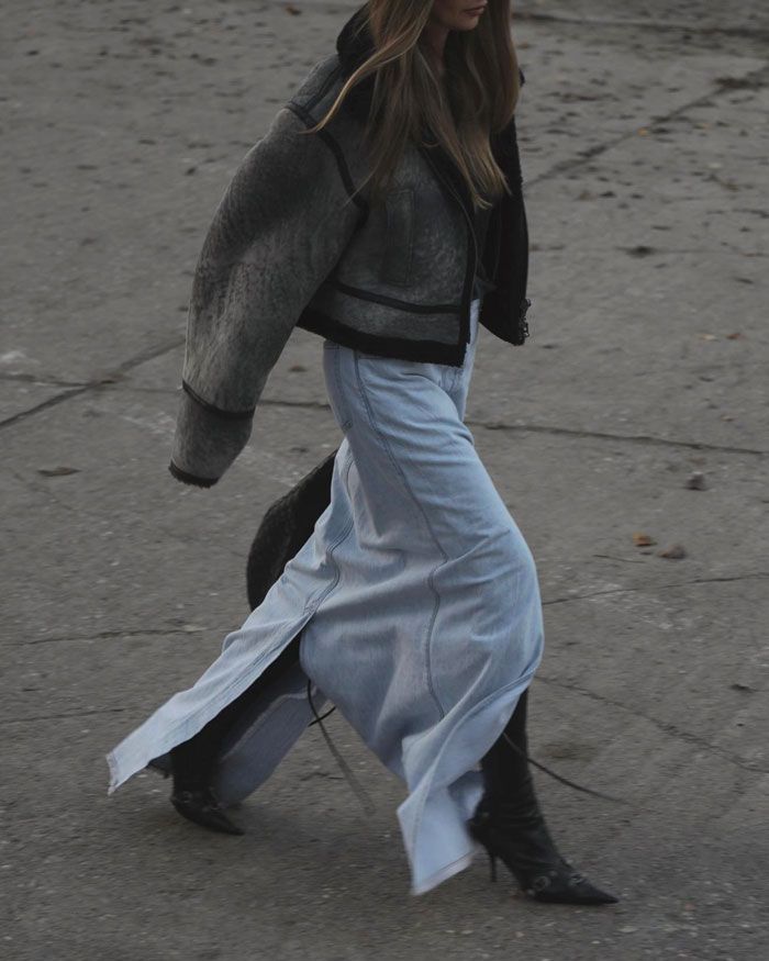 Fashionable woman in oversized jacket, long skirt, and boots walking on a textured urban surface. Stylish streetwear.