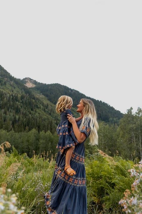 Mother and daughter in matching dresses enjoying a scenic mountain view together, surrounded by lush green forest.