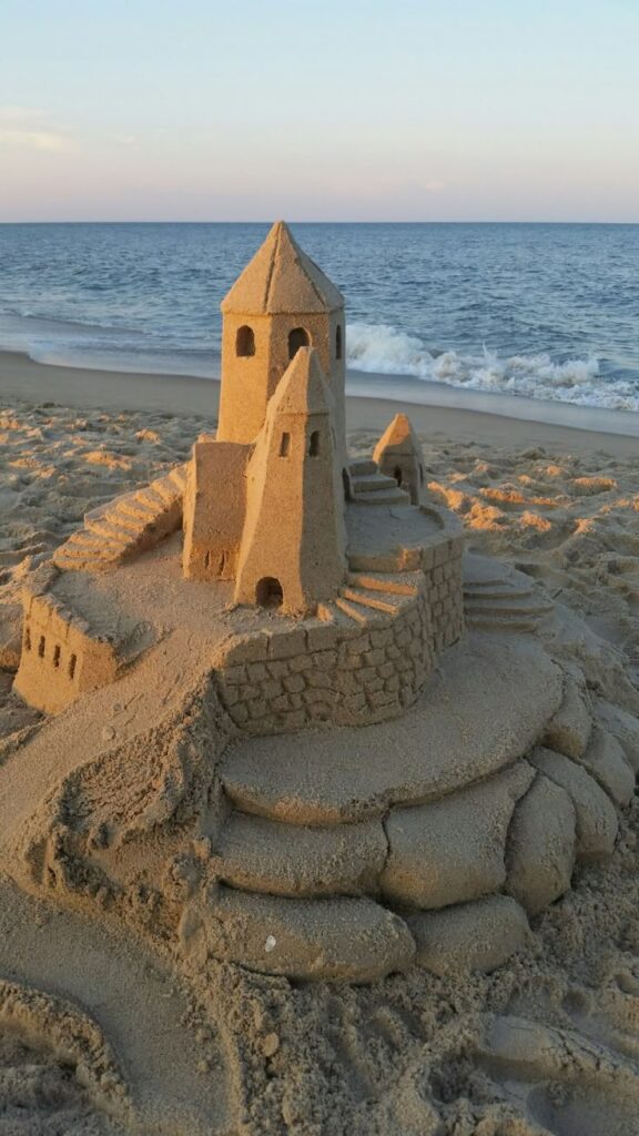 Detailed sandcastle on a beach near ocean waves under a clear sky.