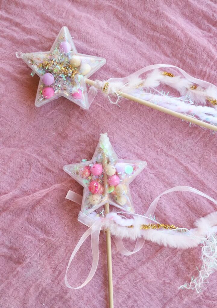 Star-shaped glitter wands with pink beads and ribbon on textured fabric background.