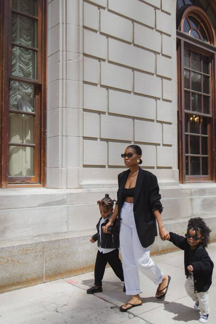 Stylish woman walks with two children in the city, all wearing chic black and white outfits.