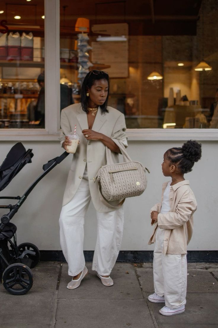 Stylish mother and daughter in matching beige outfits at a café, with stroller and milkshake.